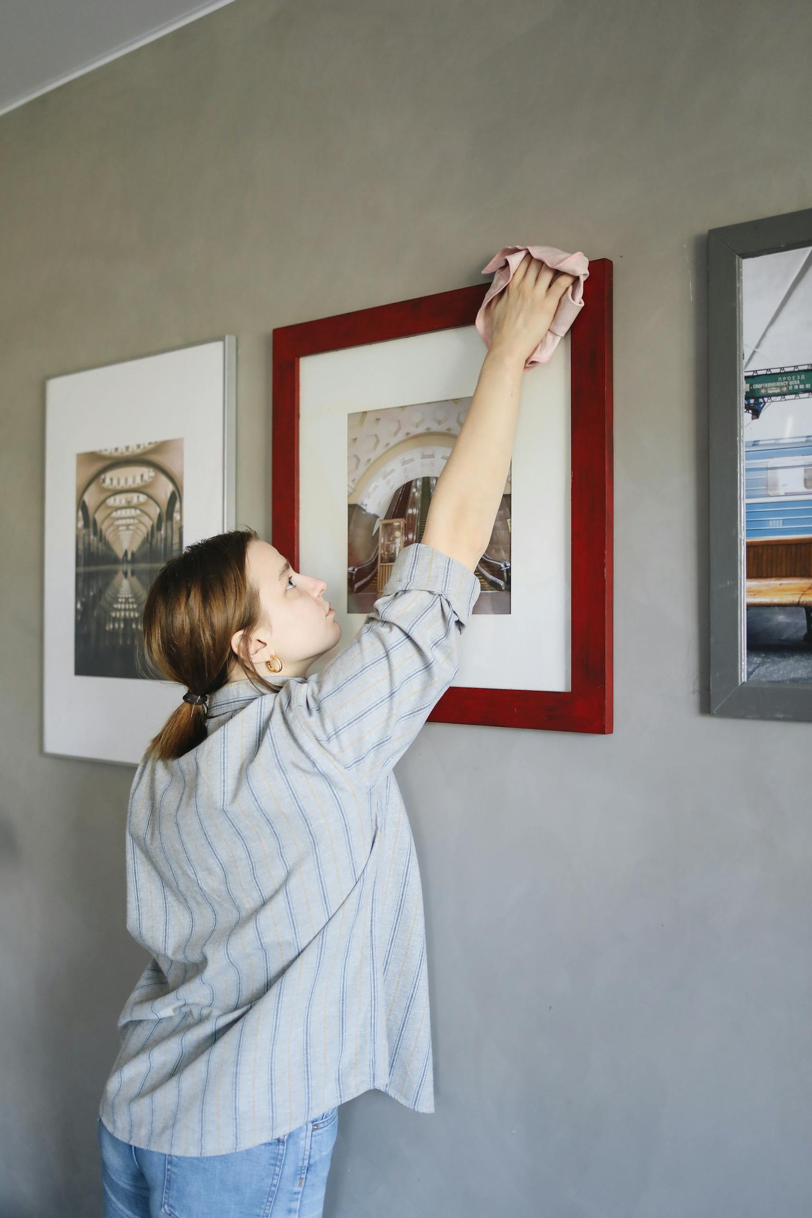 A woman cleans framed pictures on a wall, showcasing a tidy home environment.